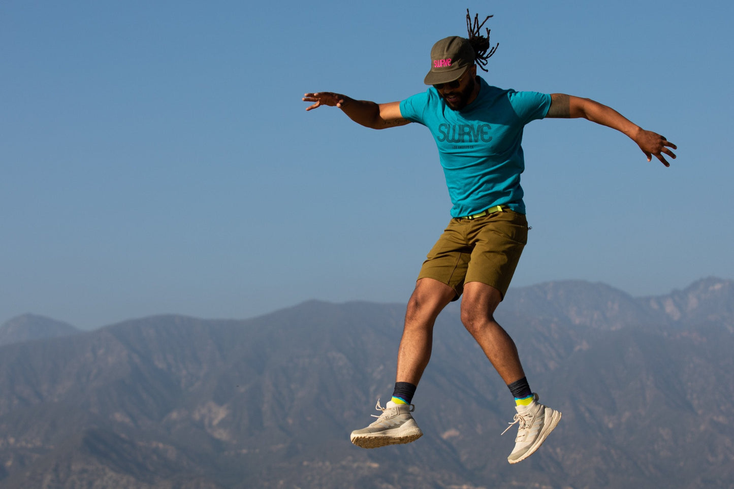 A model jumping in a classic cotton/poly 1968 swrve logo t-shirt in cyan.